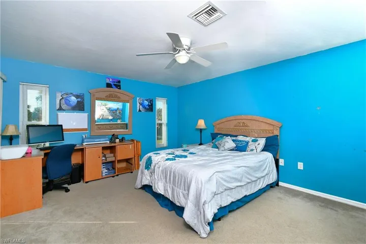 Carpeted bedroom featuring an office area, multiple windows, and a ceiling fan