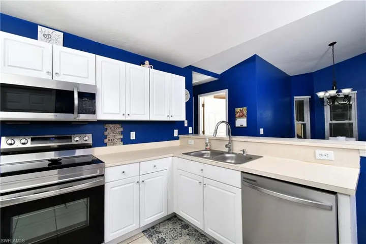 Kitchen featuring appliances with stainless steel finishes, white cabinetry, light countertops, and decorative light fixtures