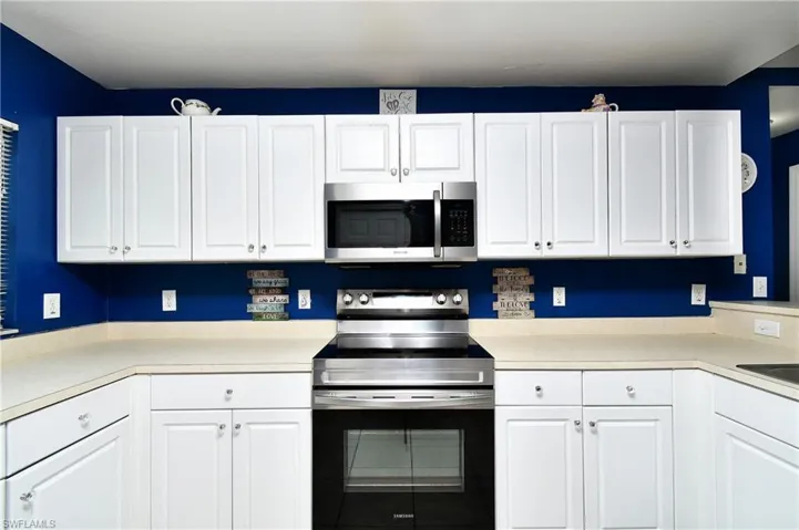 Kitchen featuring stainless steel appliances, light countertops, and white cabinetry