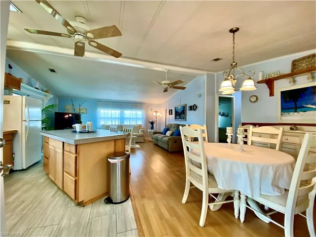 OPEN FLOOR PLAN. VIEW FROM ENTRANCE DOOR. Dining room featuring vaulted ceiling, light wood-type flooring, and ceiling fan with notable chandelier
