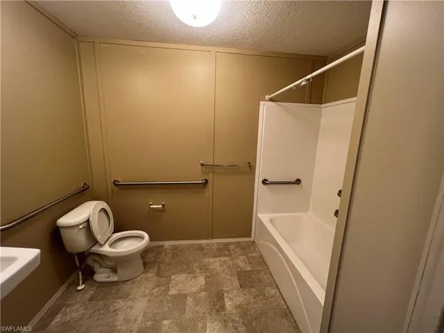 Bathroom featuring shower / bathing tub combination, tile flooring, toilet, and a textured ceiling