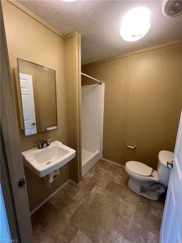 Bathroom featuring tile flooring, walk in shower, a textured ceiling, sink, and toilet