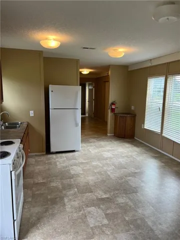 Kitchen featuring sink, a textured ceiling, white appliances, and light tile floors