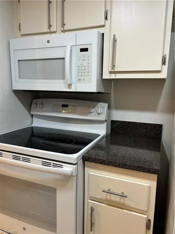 Kitchen featuring white range oven, dark countertops, and white cabinets