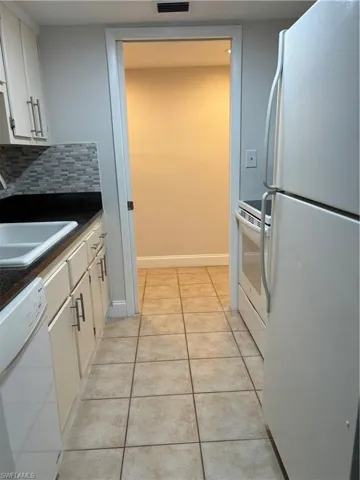 Kitchen featuring fridge, dark countertops, dishwashing machine, light tile patterned floors, and decorative backsplash