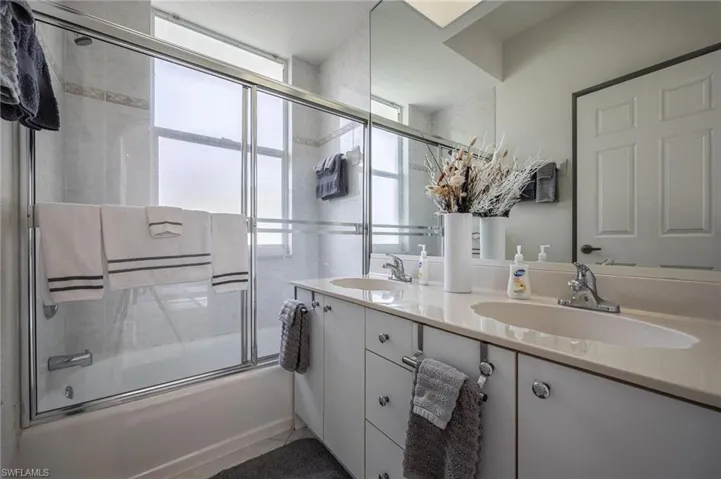 Bathroom featuring combined bath / shower with glass door and double vanity