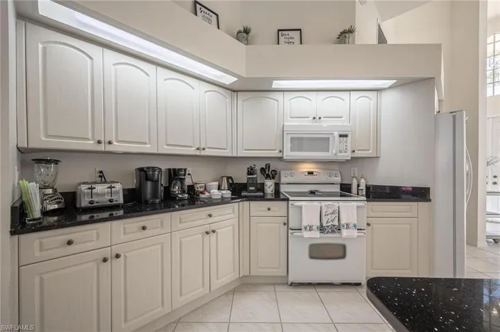 Kitchen featuring white appliances, dark stone countertops, white cabinets, a high ceiling, and light tile patterned flooring