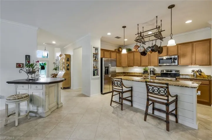 Kitchen with a kitchen breakfast bar, brown cabinets, ornamental molding, appliances with stainless steel finishes, and a center island with sink