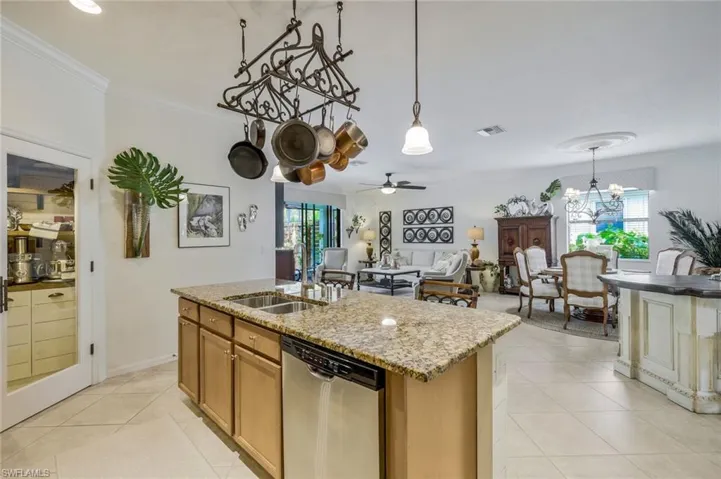 Kitchen featuring ornamental molding, a chandelier, dishwasher, a center island with sink, and light stone countertops