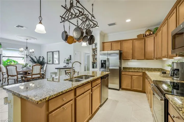 Kitchen with light stone counters, brown cabinets, ornamental molding, a chandelier, and recessed lighting