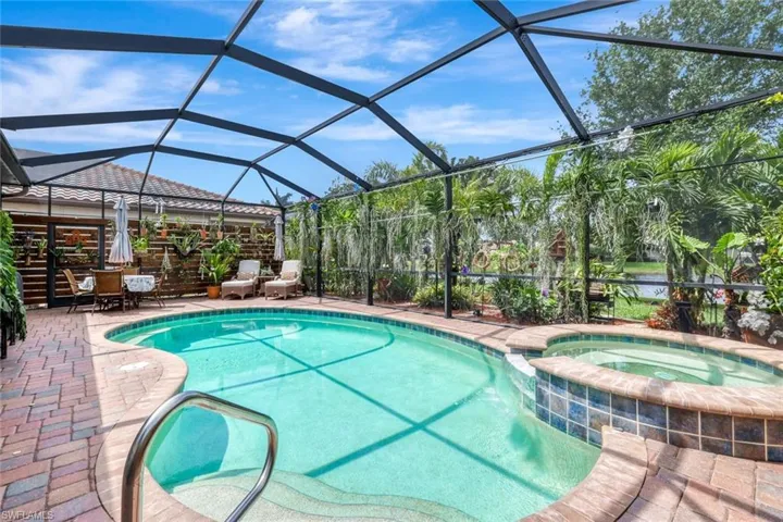 View of swimming pool featuring a pool with connected hot tub, a sunroom, glass enclosure, and a patio