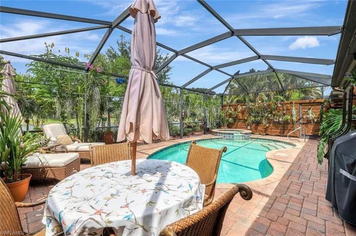View of swimming pool featuring a sunroom, a pool with connected hot tub, glass enclosure, outdoor dining area, and a grill