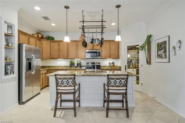 Kitchen featuring brown cabinetry, stainless steel appliances, dark stone countertops, a kitchen bar, and ornamental molding