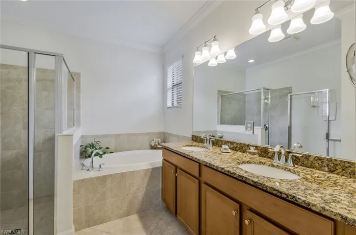 Bathroom featuring a garden tub, a shower stall, double vanity, crown molding, and light tile patterned floors