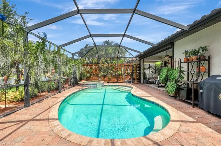 View of swimming pool featuring a sunroom, a lanai, a patio area, a pool with connected hot tub, and a grill