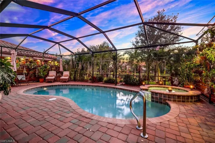 View of pool featuring glass enclosure, a sunroom, a pool with connected hot tub, and a patio