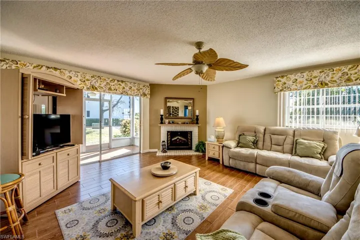Living area with wood-look ceramic tiled floors, a textured ceiling, ceiling fan, and an electric brick fireplace