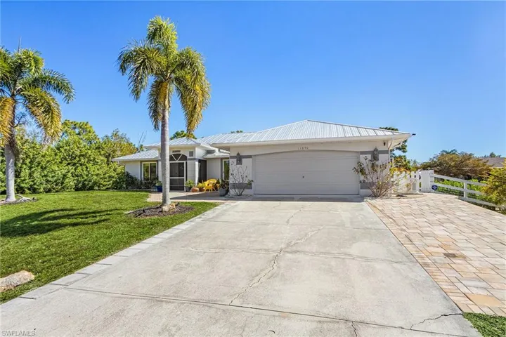 Ranch-style home with a garage, a metal roof, driveway, and stucco siding
