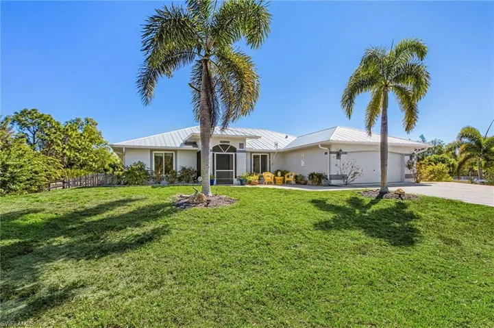 Single story home featuring a garage, a standing seam roof, a front lawn, and driveway