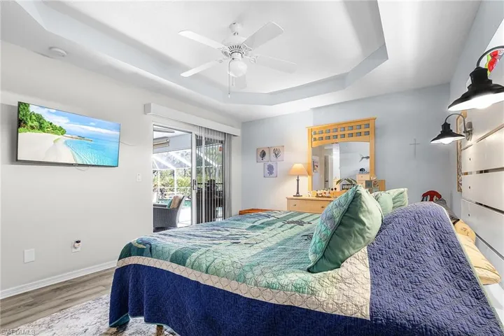 Bedroom featuring a tray ceiling, access to exterior, light wood finished floors, ceiling fan, and a sunroom