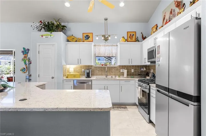 Kitchen with stainless steel appliances, white cabinets, tasteful backsplash, light tile patterned flooring, and hanging light fixtures