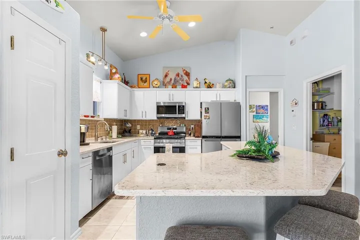 Kitchen with backsplash, ceiling fan, stainless steel appliances, lofted ceiling, and a breakfast bar