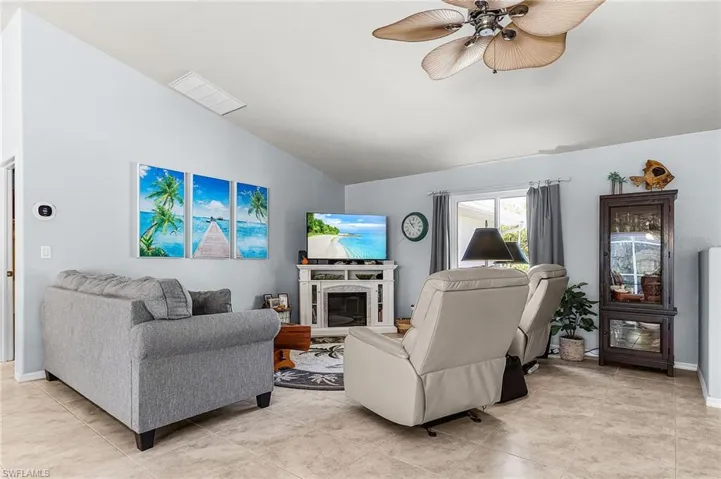 Living room featuring lofted ceiling, a ceiling fan, a glass covered fireplace, and light tile patterned floors