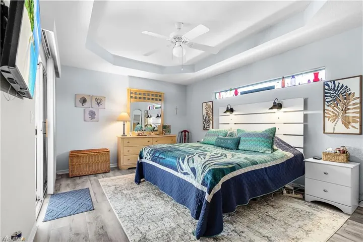 Bedroom featuring a raised ceiling, a ceiling fan, and light wood-style flooring