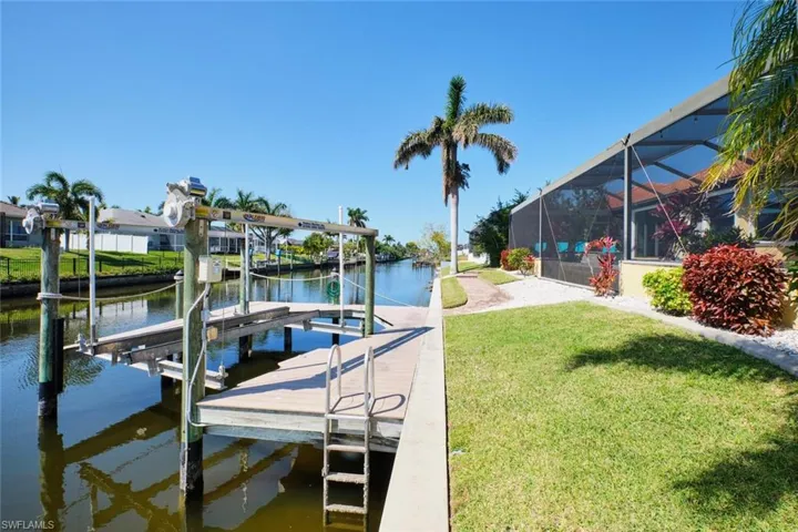 Dock area with glass enclosure, a lawn, a water view, and boat lift