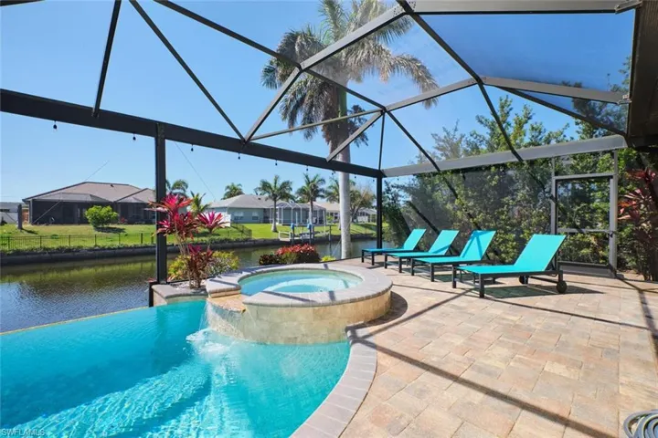 View of swimming pool with glass enclosure, a pool with connected hot tub, a patio, and a water view