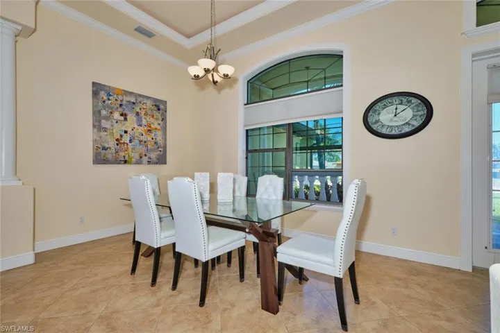 Dining area with tile patterned floors, a notable chandelier, ornamental molding, decorative columns, and baseboards