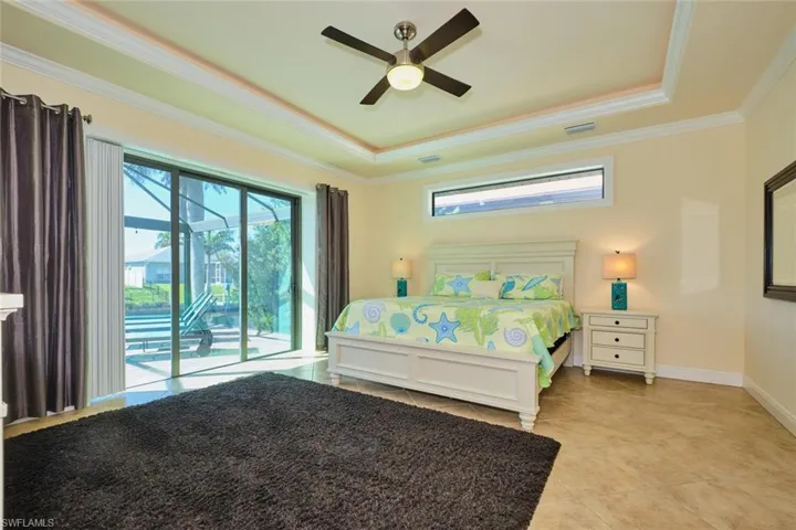 Bedroom featuring light tile patterned flooring, crown molding, a tray ceiling, and access to outside