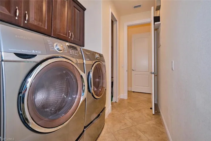 Washroom with visible vents, washer and dryer, cabinet space, light tile patterned floors, and baseboards