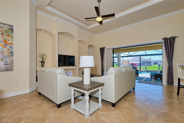 Living area featuring light tile patterned floors, a ceiling fan, baseboards, a tray ceiling, and crown molding