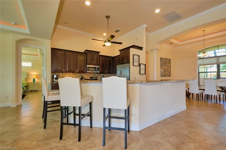 Kitchen featuring arched walkways, dark brown cabinetry, appliances with stainless steel finishes, pendant lighting, and backsplash