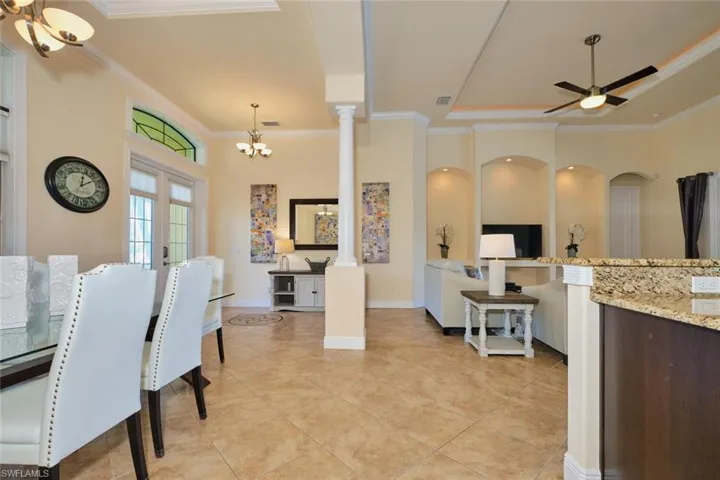 Dining space with crown molding, decorative columns, ceiling fan with notable chandelier, and baseboards