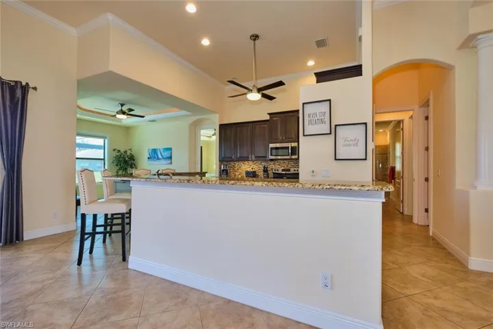 Kitchen featuring stainless steel microwave, crown molding, dark brown cabinetry, arched walkways, and a ceiling fan