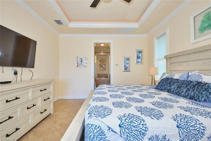 Bedroom featuring a raised ceiling, light tile patterned floors, crown molding, and visible vents