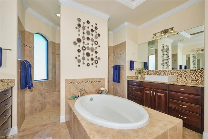 Full bathroom featuring tile patterned flooring, a walk in shower, a garden tub, ornamental molding, and vanity