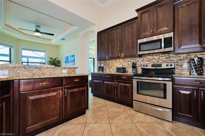 Kitchen featuring light tile patterned floors, a ceiling fan, stainless steel appliances, a raised ceiling, and backsplash