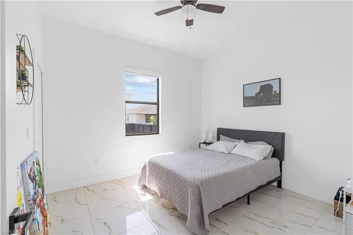 Room featuring a square window, a ceiling fan with dark wood-finish blades, and large format tile flooring