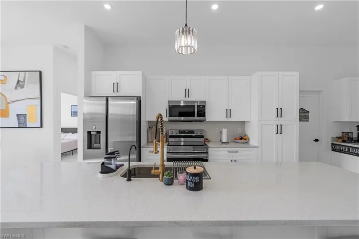 Spacious kitchen featuring an expansive island with a built-in sink and two-tone faucet, white shaker cabinetry with dark hardware, stainless steel appliances, and recessed lighting