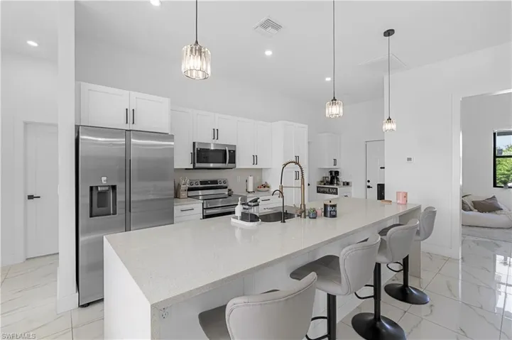 Modern kitchen featuring white cabinetry, stainless steel appliances, a large island with a surface suitable for seating, pendant lighting, and polished tile flooring