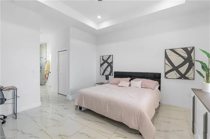 Spacious room featuring large format tile flooring, a tray ceiling, recessed lighting, white walls, and a bi-fold closet door