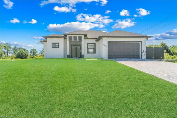 Contemporary single-story residence featuring a smooth stucco exterior, a dark gray overhead garage door, a paved driveway, and an expansive green lawn