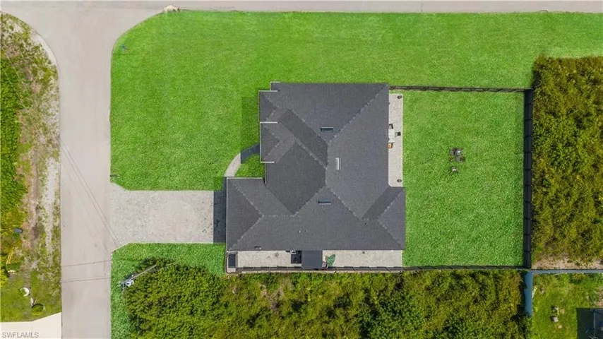Overhead perspective showcasing the property's dark shingle roof, expansive green lawn, stone paver patio, and paved driveway