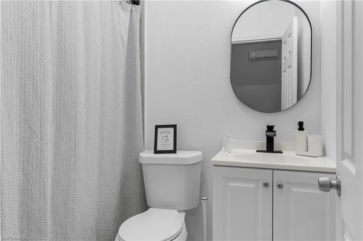 Bathroom featuring a white vanity with a light-toned countertop, a black faucet, and an oval-shaped mirror