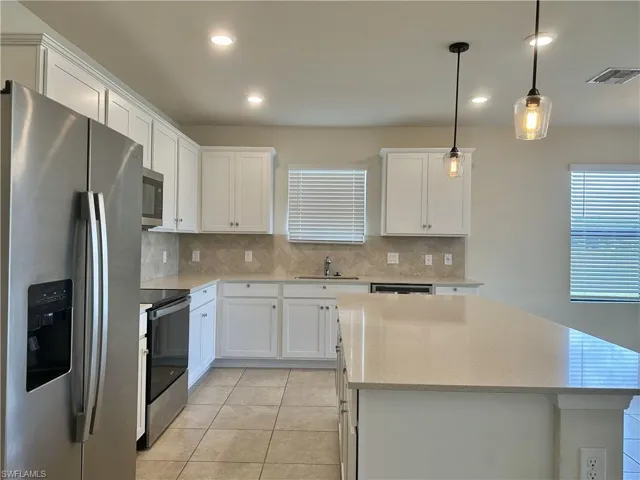 Kitchen with stainless steel appliances, decorative light fixtures, white cabinets, light stone counters, and backsplash