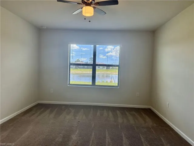 Empty room featuring dark colored carpet and ceiling fan