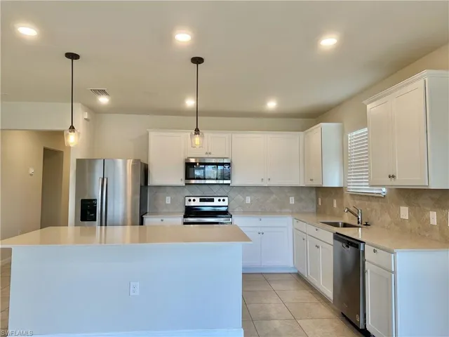 Kitchen featuring appliances with stainless steel finishes, white cabinetry, decorative backsplash, hanging light fixtures, and recessed lighting
